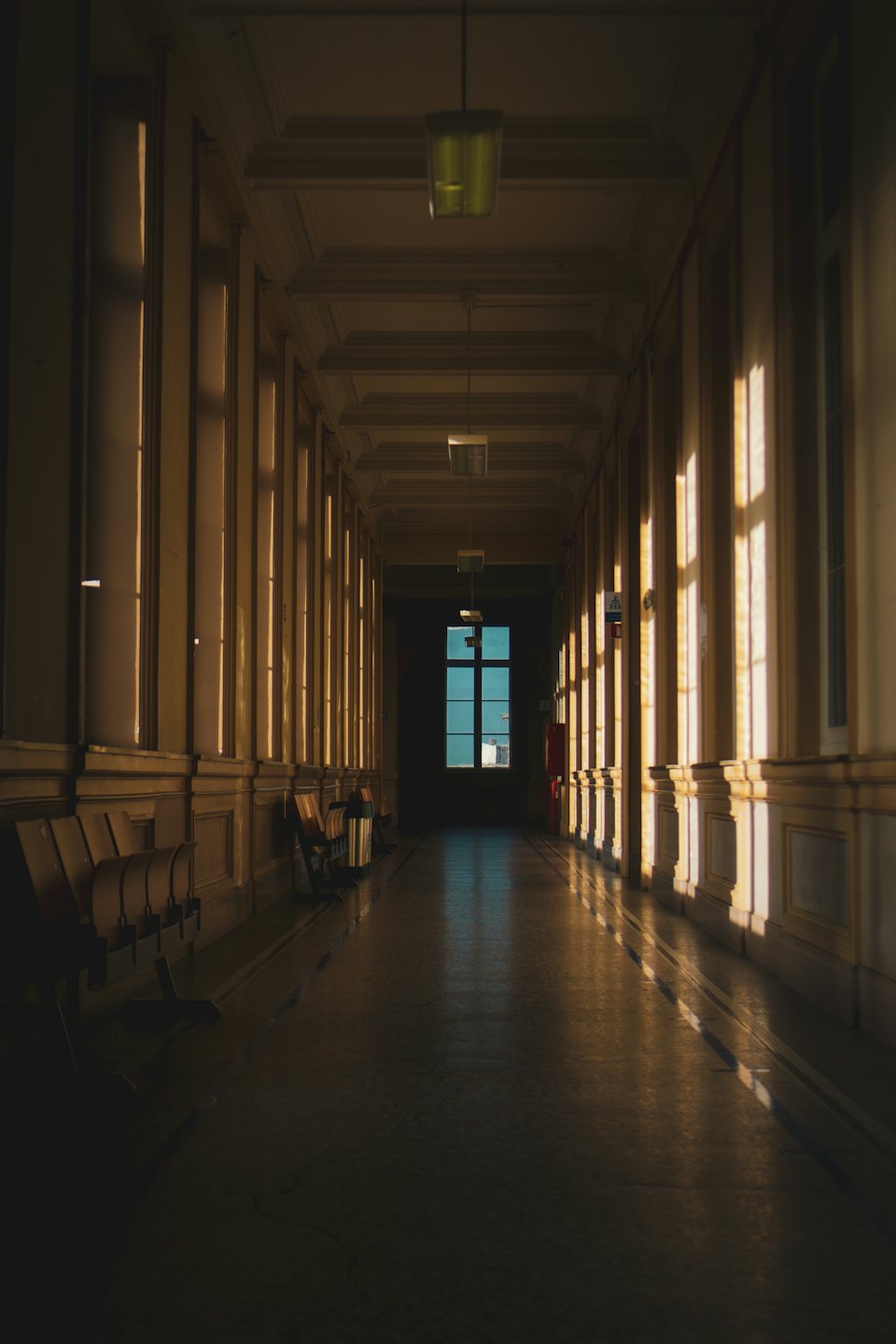 Sunlight streams across a long hallway with wooden bench seating.